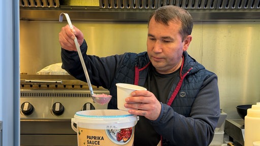 Imbissbetreiber Michael Oberst steht mit einer Kelle in seinem Foodtruck und füllt Suppe in eine Einwegverpackung.