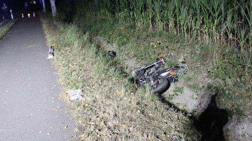 Ein Motorrad liegt nachts in einem Straßengraben neben einer Landstraße in Espelkamp im Kreis Minden-Lübbecke. Die Unfallstelle ist im Hintergrund abgesichert.