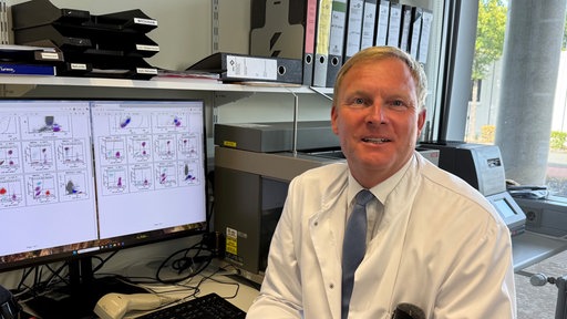 Professor Gunter Aßmann von der Uniklinik in Minden sitzt an seinem Schreibtisch und blickt freundlich in die Kamera 