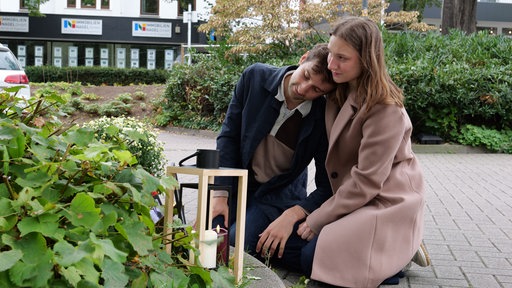 Ferris und Stella Fechner knien vor einer Kerze am Bahnhofsparkplatz in Bad Oeynhausen