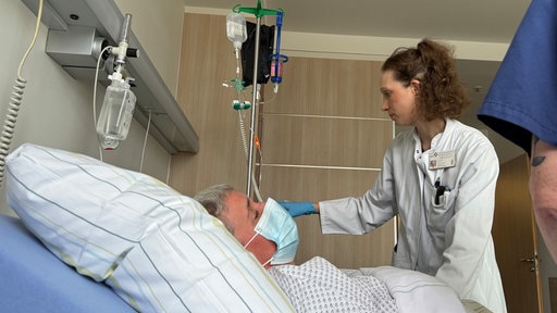 Ein Patient liegt im Bett, während sich das Pflegepersonal um ihn kümmert