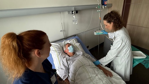 Ein Patient liegt im Bett, während sich das Pflegepersonal um ihn kümmert
