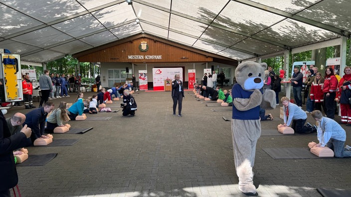 In einer Halle finden moderierte Übungen für Herzdruckmassagen an Plastikpuppen statt.