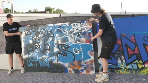 Zwei Jugendliche stehen vor SCP Graffiti Wand.