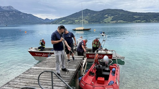 Mehrere Einsatzkräfte stehen auf dem Steg am See und steigen in Bote