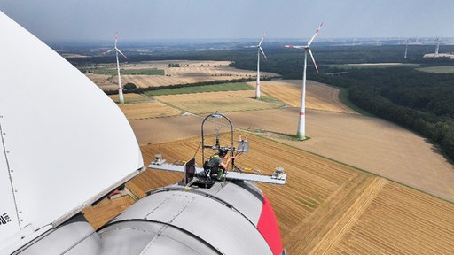 Ein WIndkraftmonteur mit Helm und Klettermontur ragt aus einer Luke und arbeitet in 135 Metern Höhe an einem Windrad.