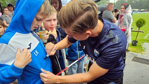 Ein Fußballspieler vom FC Paderborn schreibt sein Autogramm auf den Pulli eines jungen Fans.
