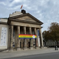 Auf dem Bild sieht man das Landestheater wie es heute aussieht. Mit sechs hohen Säulen vor dem Eingang. An den Säulen hängt ein Banner in Regenbogenfarben mit der Aufschrift "Für Respekt und Vielfalt" anlässlich des 200. Jubiläums.