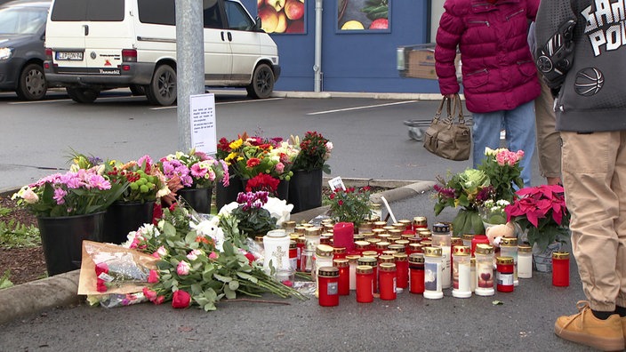 Grablichter und Blumen stehen auf dem Parkplatz eines Supermarkts in Lemgo
