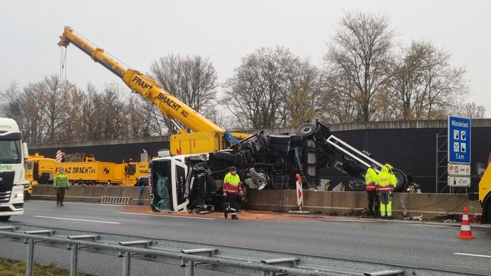 Ein umgekippter LKW liegt auf einer Mittelleitplanke auf einer Autobahn: Im Hintergrund ist ein Kran zu sehen