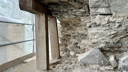 Zwei Holzpfeiler halten einen Steinblock der Fassade 