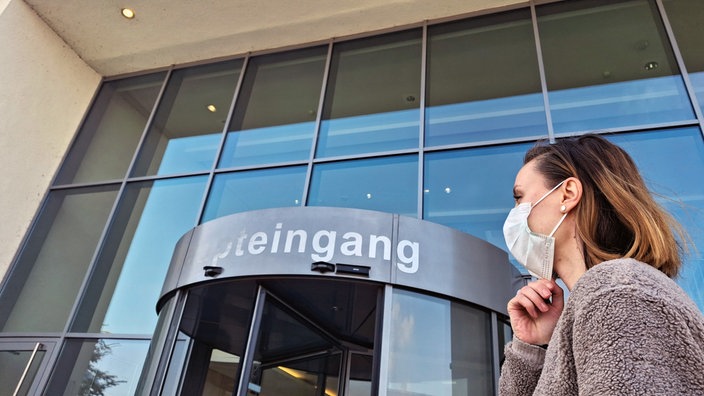 Eine Frau mit Maske vor einem Krankenhaus