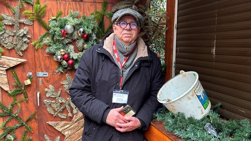 Ein Mann steht vor einer weihnachtlich geschmückten Holzhütte