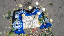 Schild mit dem Satz: Unsere Gedanken sind bei euch! liegt auf dem Boden. Ein Armenia-Bielfefeld-Schal rahmt das Schild und Grabkerzen stehen darum.