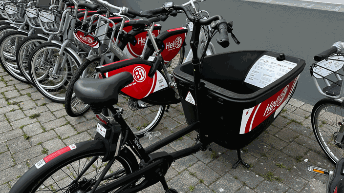 Einige Leihfahrräder und ein Lastenrad stehen am Straßenrand