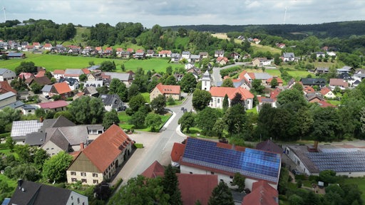 Ansicht vieler Häuser und einer Hauptstraße von oben. Auf einigen Dächern der Häuser sind Solar-Anlagen.