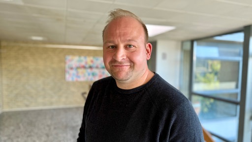 Ein Mann in schwarzem Sweatshirt steht in einer Schule