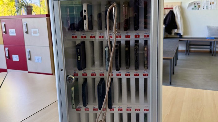 Das Handyhotel hat mehrere Fächer, in dem Handys liegen. Diese sind hinter einer Glaswand verschlossen. 