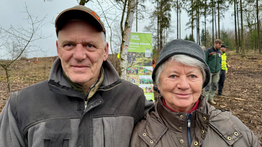 Agatha und Thomas Sondermann gucken in die Kamera. Im Hintergrund läuft die Baumpflanz-Aktion.