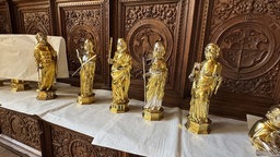 Fünf goldene Figuren stehen auf einem Altar vor einer schmuckvollen Holzfassade.