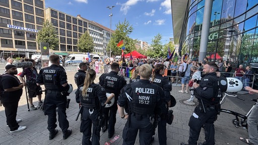 Eine Gruppe Polizisten steht vor einer Gruppe Demonstranten mit Regenbogenfahnen 
