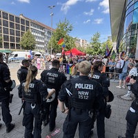 Eine Gruppe Polizisten steht vor einer Gruppe Demonstranten mit Regenbogenfahnen 