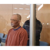 Der Angeklagte steht im Gerichtssaal. Hinter einer Säule steht zur Bewachung ein Wächter.