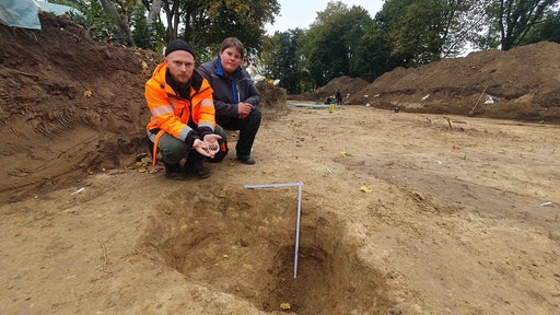 Zwei Personen vor einem circa 50 cm tiefen Raubgrabungsloch