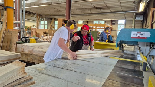 Zwei Männer arbeiten in einer Werkstatt mit Holzbrettern.