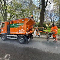Ein oranegens kleines Fahrzeug mit einem Schlauch, das Schlaglöcher auffüllt. 
