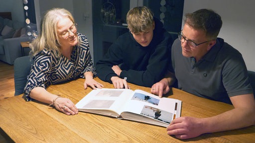 Eine Familie sitzt an einem Tisch und blättert durch ein Fotoalbum
