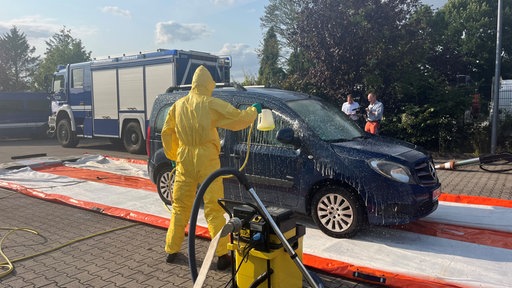 Ein Auto wird von einer Person in gelbem Schutzanzug eingesprüht