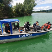 Polizeitaucher sitzen auf einem Sonarboot, das auf einem Kiesteich nahe Porta Westfalica treibt