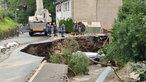 Männer vom Technischen Hilfswerk stehen um eine stark beschädigte Straße