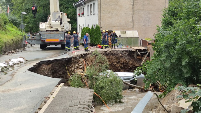Männer vom Technischen Hilfswerk stehen um eine stark beschädigte Straße