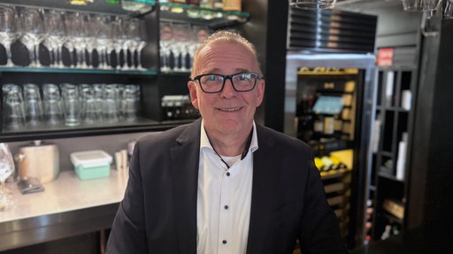Bernd Tönsing steht lächelnd vor einer Bar