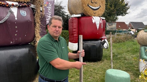ein Mann vor Strohballen-Puppen zeigt auf einen leeren Platz