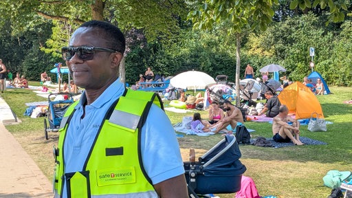 Ein Sicherheitsmann in gelber Signalwester überblickt die Wiesen im Freibad Verl.