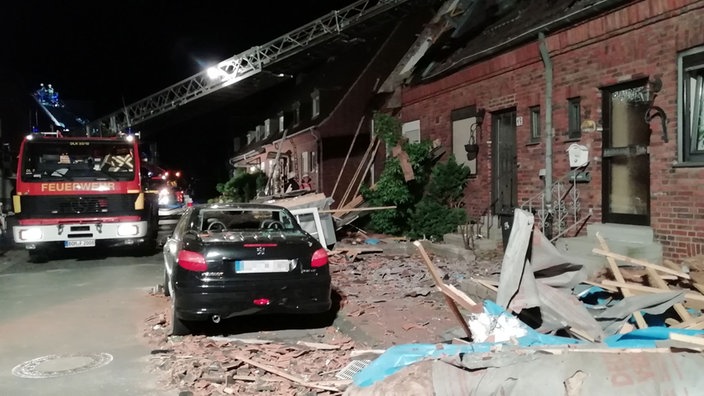 Vor einem beschädigtem Haus steht ein Pkw und ein Auto der mit Drehkran