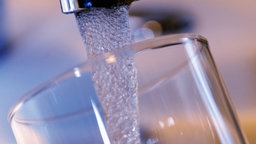 Trinkwasser läuft aus einem Wasserhahn in ein Glas.