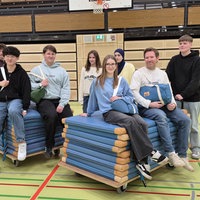 Die Schülergruppe und ihr Lehrer sitzen auf den Turnmatten