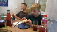 Zwei Jungen sitzen an einem Tisch und essen etwas