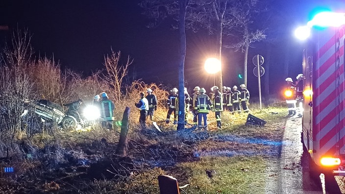 Links im Graben liegt ein demoliertes Fahrzeug, rechts daneben stehen Einsatzkräfte der Feuerwehr Brilon