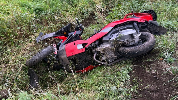 Ein rotes dreirädriges Motorad liegt auf einem Wiesenstück.