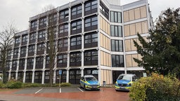 Zwei Einsatzwagen der Polizei stehen vor einem modernen Gebäude