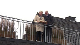 Ehepaar Leissing steht auf einem Balkon und schaut in ein Album.