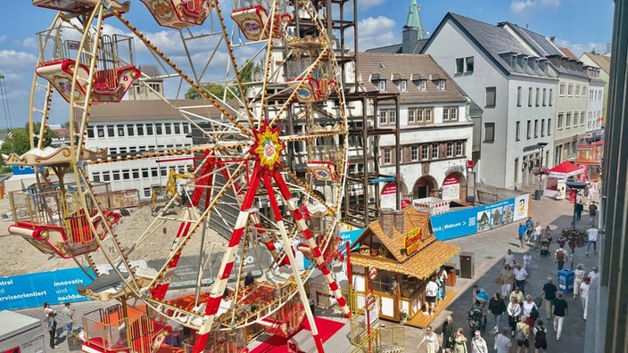 Ein Riesenrad steht in einer Fußgängerzone, dort laufen viele Besucher.