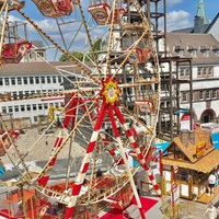 Ein Riesenrad steht in einer Fußgängerzone, dort laufen viele Besucher.