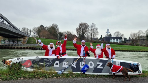 Fünf Menschen als Weihnachtsmänner verkleidet mit einem SUP-Board und einem Hund