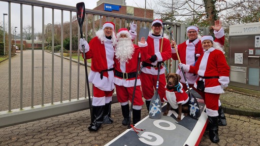 Fünf Menschen und ein Hund - allesamt als Weihnachtsmänner verkleidet - mit einem SUP